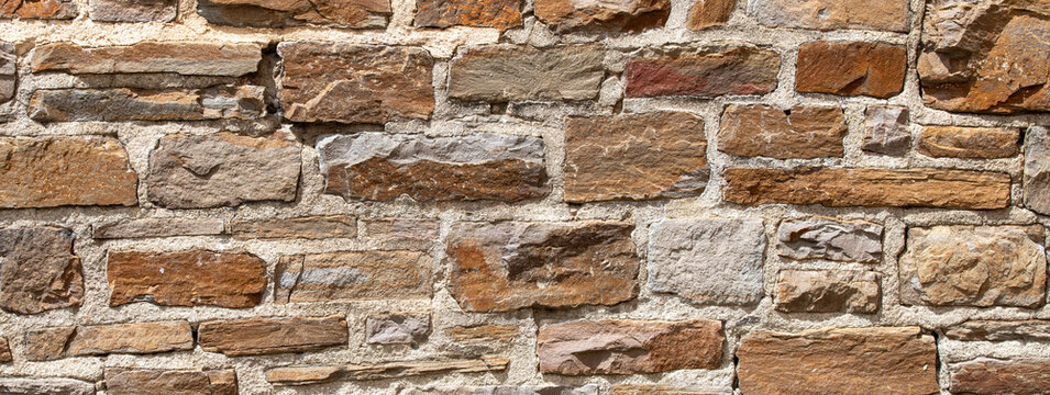 Old rustic natural stone wall background built with uneven brown granite bricks