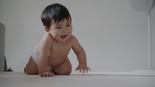 Adorable infant wearing diaper sitting on mat in bright room, growth concept.