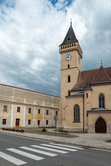 Obraz premium Gothic Church of St. John the Baptist in Sabinov, Slovakia, with its medieval bell tower beneath dramatic storm clouds, standing in the heart of the town's historic square.