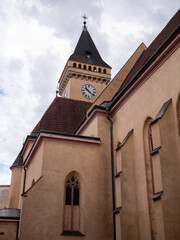 Fototapeta premium Close-up view of the Gothic Church of St. John the Baptist in Sabinov, Slovakia, highlighting its medieval clock tower and historic architecture beneath a bright, cloud-filled sky.