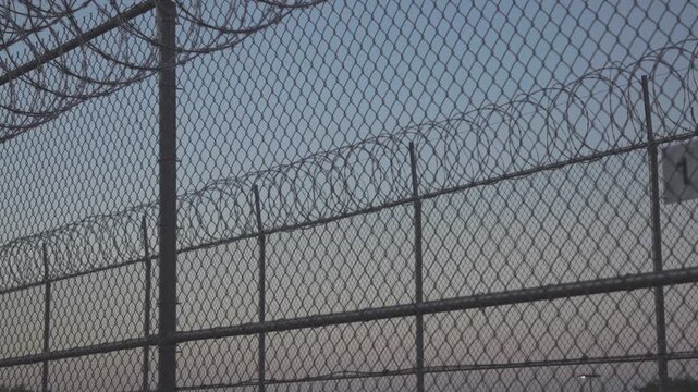 Security chain link fence with barbed wire against twilight sky.
