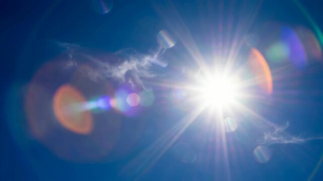 Bright sun shining in a clear blue sky with lens flare and light reflections