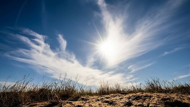 Bright sun shining over dry grassland and clear blue sky with wispy clouds on a sunny day