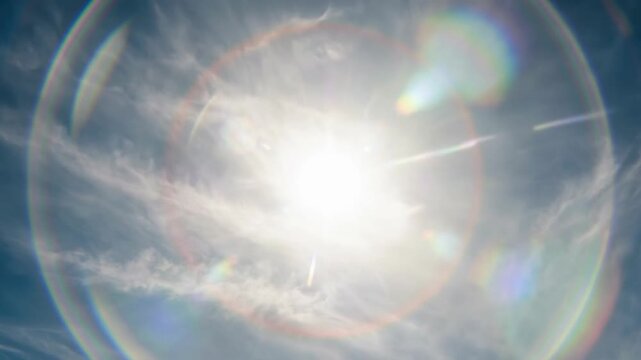 Bright sun with colorful halo and light reflection in blue sky with clouds