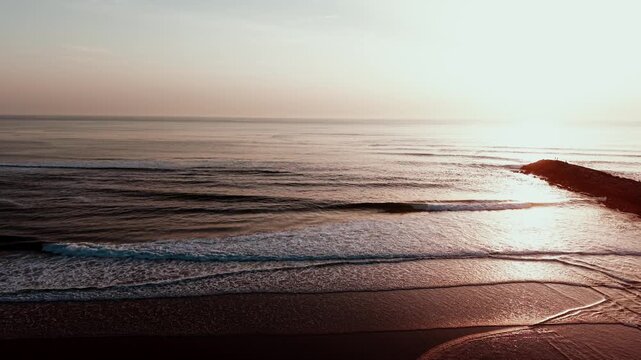Sun reflects on calm sea and gentle waves lapping sandy shore at Maceda Beach in Ovar Portugal