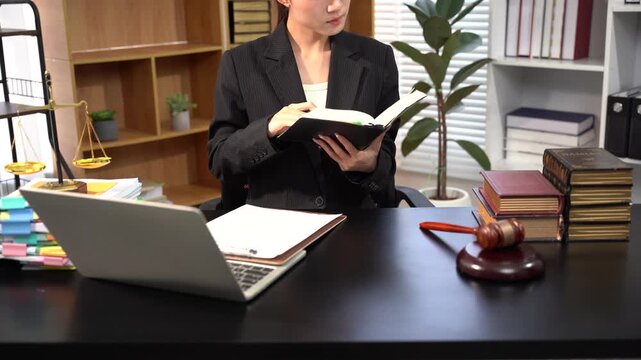 Lawyer Studying Case Files: A professional female lawyer intently studies a book at her desk, surrounded by legal documents, a gavel, and stacks of law books in a well-appointed office.