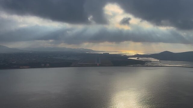 An immersive pilot's eye view of the coastal Ibiza airport (IBZ) runway at sunset, with a turbulent sky with clouds and the sunlight reflected on the sea.