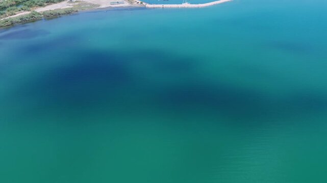 Beautiful drone shot flying over abstract turquoise and emerald sea water in Kopraina, Amvrakikos Gulf, Greece. Features natural seabed dark shadow patterns and calm ripples on a sunny summer daytime.