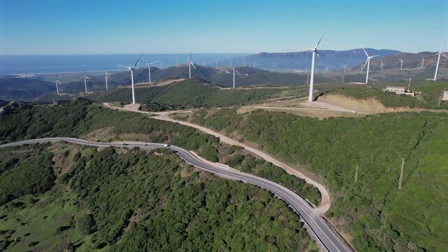 Aerial drone view of wind turbines on green hills with winding road