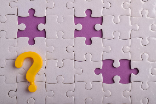 Yellow question mark on a white jigsaw puzzle with missing pieces on a purple background, symbolizing questions, uncertainty, problem solving, critical thinking, and finding solutions.