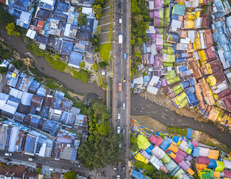 Aerial view of the colorful Rainbow Village in Malang, Indonesia, showcasing vibrant houses, a busy road, and surrounding greenery