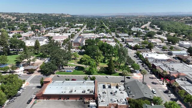 Aerial drone view of Downtown City Park in Paso Robles, California, located near US Route 101 surrounded by streets, trees, downtown buildings, and Central Coast wine country scenery on a sunny day