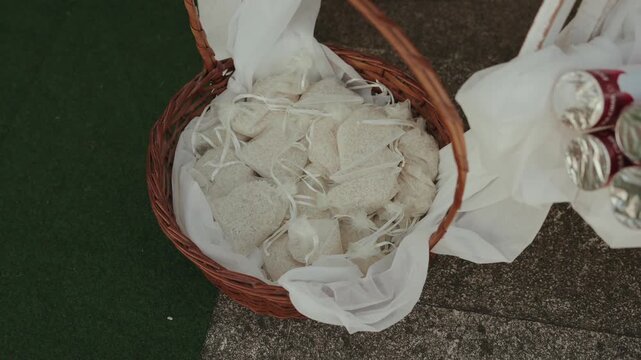Small tied fabric bags line white cloth inside wicker basket at outdoor gathering