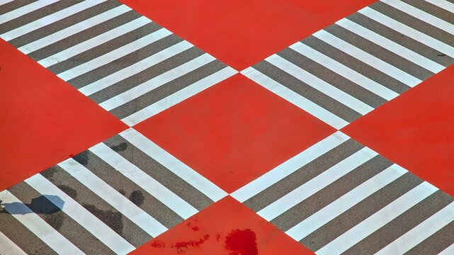 An aerial view of the bold red and white diagonal patterned crosswalk in Seoul with a single pedestrian crossing visible.