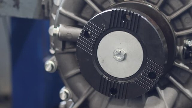 ​Detailed view of a metallic vehicle transmission pulley flange bolted on a mechanical drive shaft mechanism inside an automotive engineering assembly workshop.