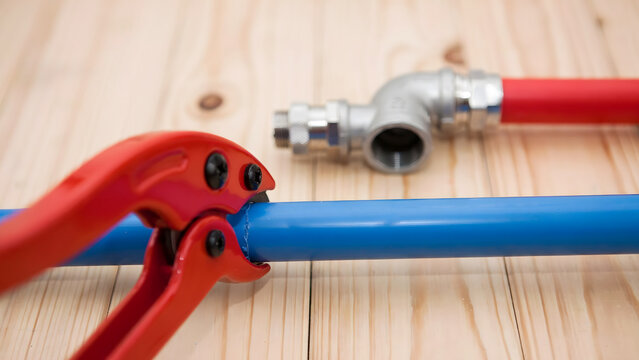 Red pipe cutting tool on a blue PEX pipe next to a metal plumbing fitting