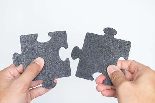 Hands Holding Two Black Jigsaw Puzzle Pieces About to Connect on White Background