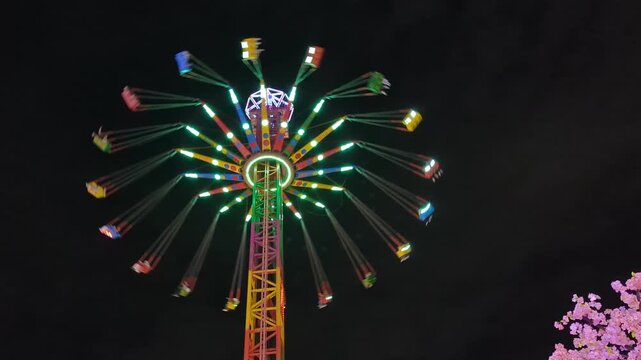 Glowing chain carousel ride spinning at night amusement park. Colorful fairground attraction spinning fast in the evening. Bright multicolored LED lights glowing on a rotating chain swinger ride.