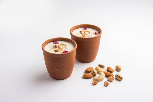 Two clay cups of traditional indian thandai garnished with nuts and rose petals beside dry fruits