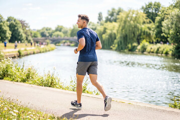Obraz premium Athletic man jogging along river path on sunny morning