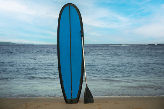 Colorful surfboard and paddle on sandy shore with gentle waves