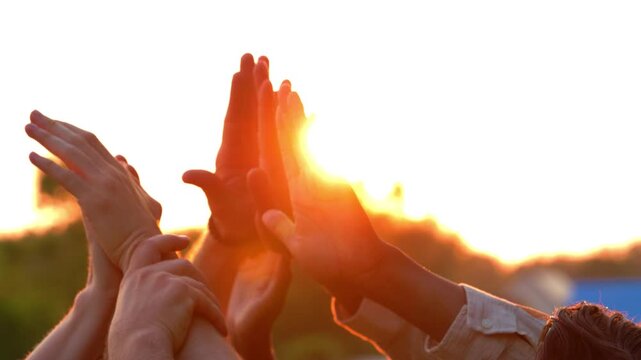 Teamwork and Unity: Diverse Hands Raised in Celebration Against a Golden Sunset Sky