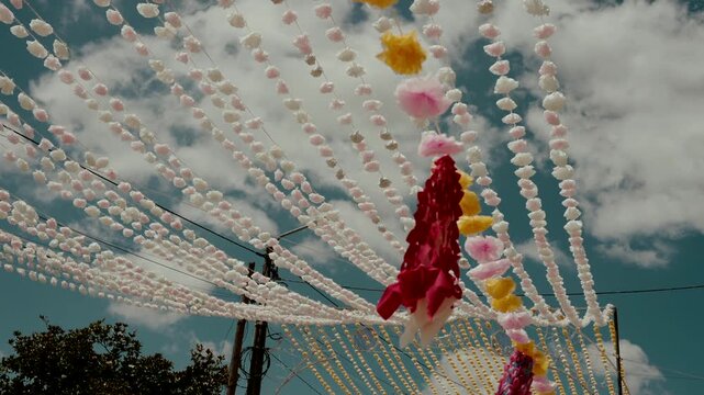 Radiating pink bead strings and a red flower streamer converge over street pole at arraial festival in Portugal