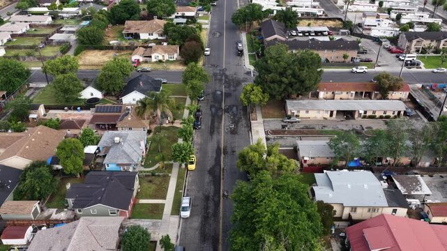 Tree-lined residential street splits Madera neighborhood in two halves, houses with solar panel rooftops and parked cars line curbs beneath California&rsquo;s clear summer sky. Aerial drone flyover shot