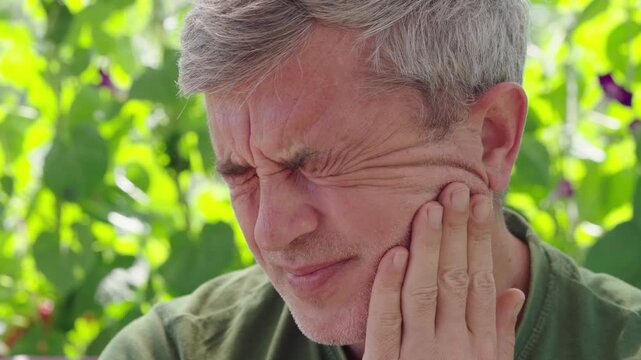 Middle-aged man suffering from severe toothache outdoors, close-up