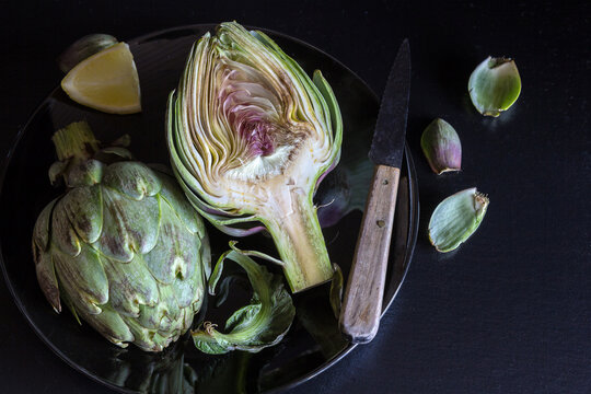 Fresh artichokes cut half with lemon and knife - dark and moody tone