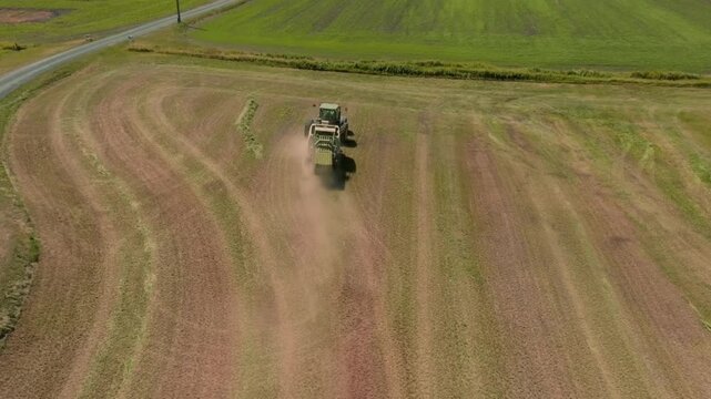 High rear aerial drone shot of a modern tractor working across productive agricultural fields in the British countryside. Elevated perspective captures powerful farming machinery cultivating the land,