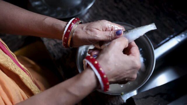 Indian married woman (only hand showing) hygienically washing fresh raw Labeo bata fish in a kitchen basin before cooking. Close-up of clean fish preparation, traditional home cooking, and food safety