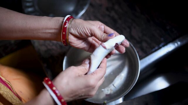 Indian married woman hygienically washing fresh raw Labeo bata fish in a kitchen basin before cooking. Close-up of clean fish preparation, traditional home cooking, and food safety.
