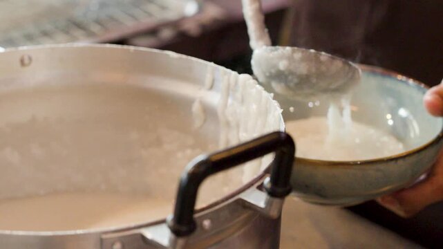 Chef Ladling Hot Asian Rice Porridge Into Ceramic Serving Bowl