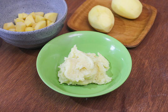 Homemade smooth mashed potatoes in green ceramic bowl on wooden table