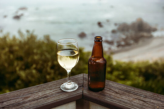A glass of white wine and a beer bottle sit on a deck