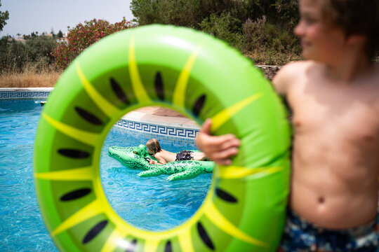 Young kid on crocodile float in pool through a ring float