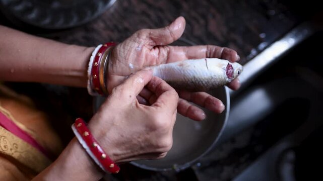 Indian married woman hygienically washing fresh raw Labeo bata fish in a kitchen basin before cooking. Close-up of clean fish preparation, traditional home cooking, and food safety.	