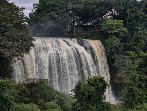Linh An Pagoda overlooking Elephant Waterfall surrounded by lush tropical forest in Da Lat, Vietnam, beneath bright blue skies with towering palms and vibrant green vegetation. Photo taken in July 202