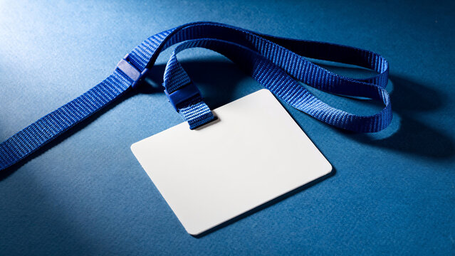 Blank white badge with blue lanyard on textured blue background, close-up, concept for event access, employee identification and security passes