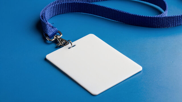 Blank white ID card with blue lanyard and metal clip on a blue background, top view, concept for access, identity and security