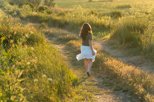 Young woman walking on a dirt path in a summer meadow at sunset