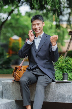 Asian businessman celebrating success with smartphone outdoors