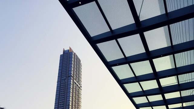 Modern skyscraper rises beside a geometric glass canopy against a clear sky.