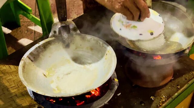 Fresh egg fries in a metal pan above a traditional charcoal cooking stove.
