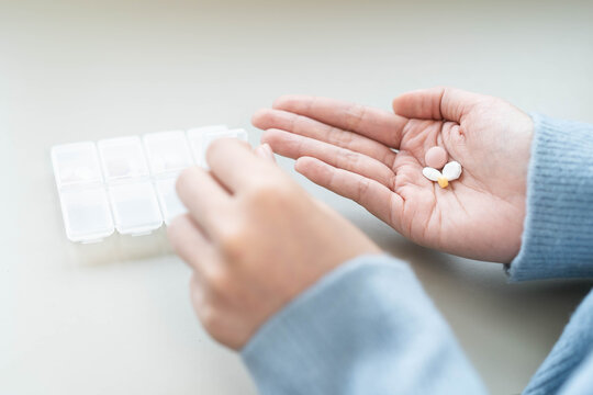 Close-up of a woman holding daily medication pills in hand with a pill organizer box.