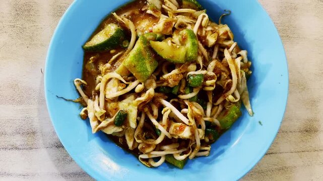 Savory stir-fried noodles with vegetables and sprouts are served on a blue plate.