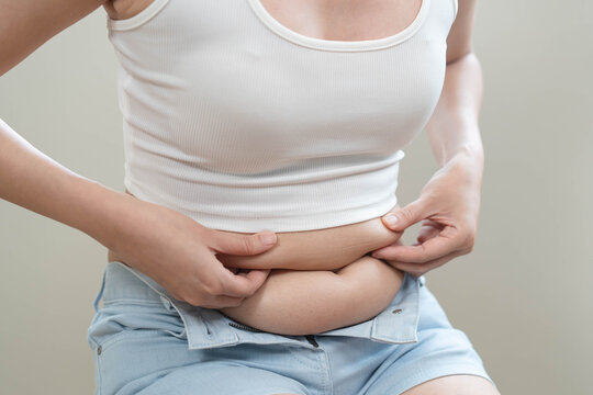 Close-up of a young woman pinching belly fat on her stomach in white crop top.
