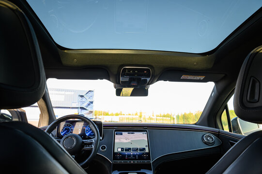 Panoramic sunroof and front dashboard view inside a modern luxury car cabin from the back seat, close up.