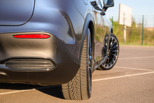 Exterior view of the rear wheel, tire, and bumper section of a modern luxury car, showcasing its tread pattern and alloy wheels, close up.